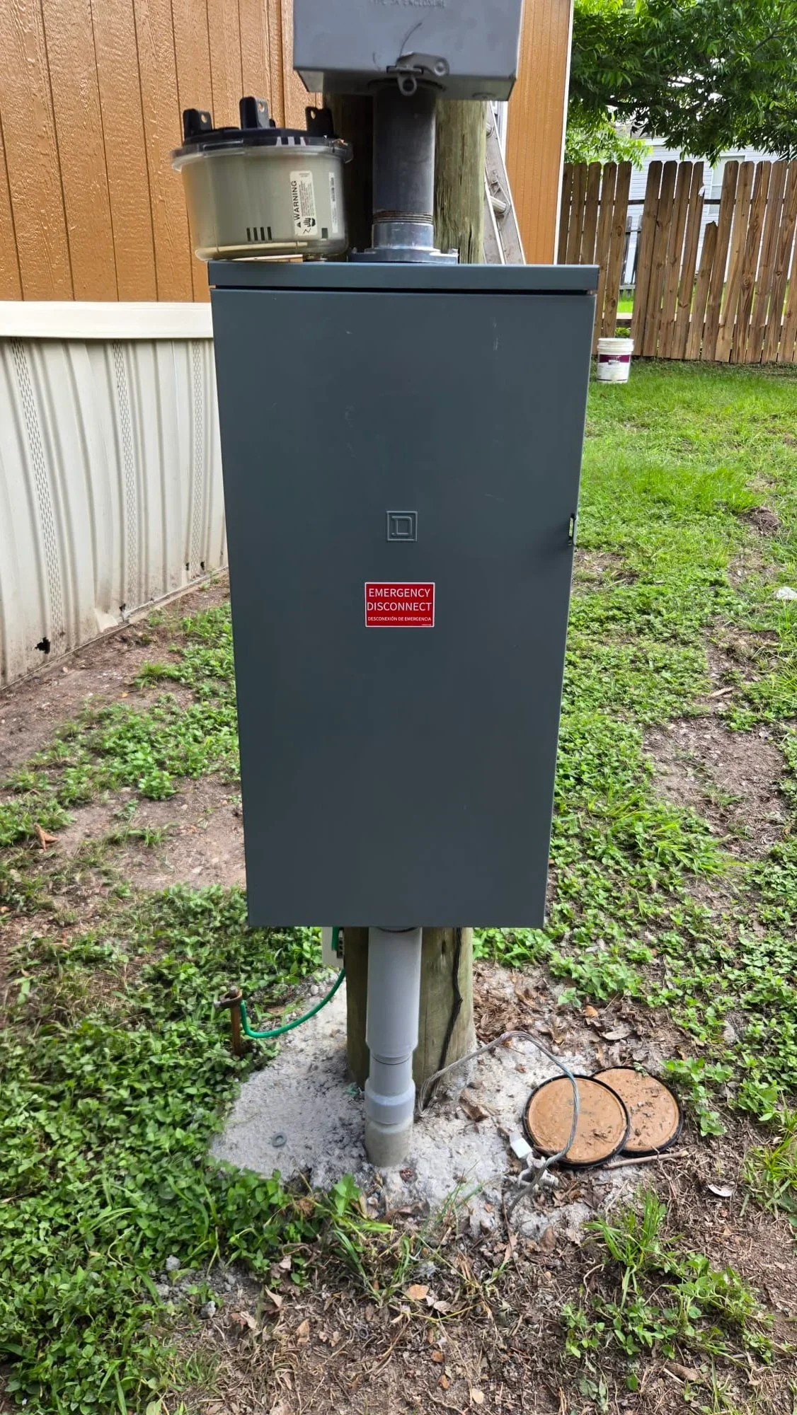 Dark metal electrical disconnect box with breaker panel mounted on wooden post with grounding