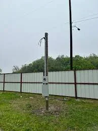 Outdoor electrical pole with mounted fixtures, conduit, and grounding hardware installed in grassy area