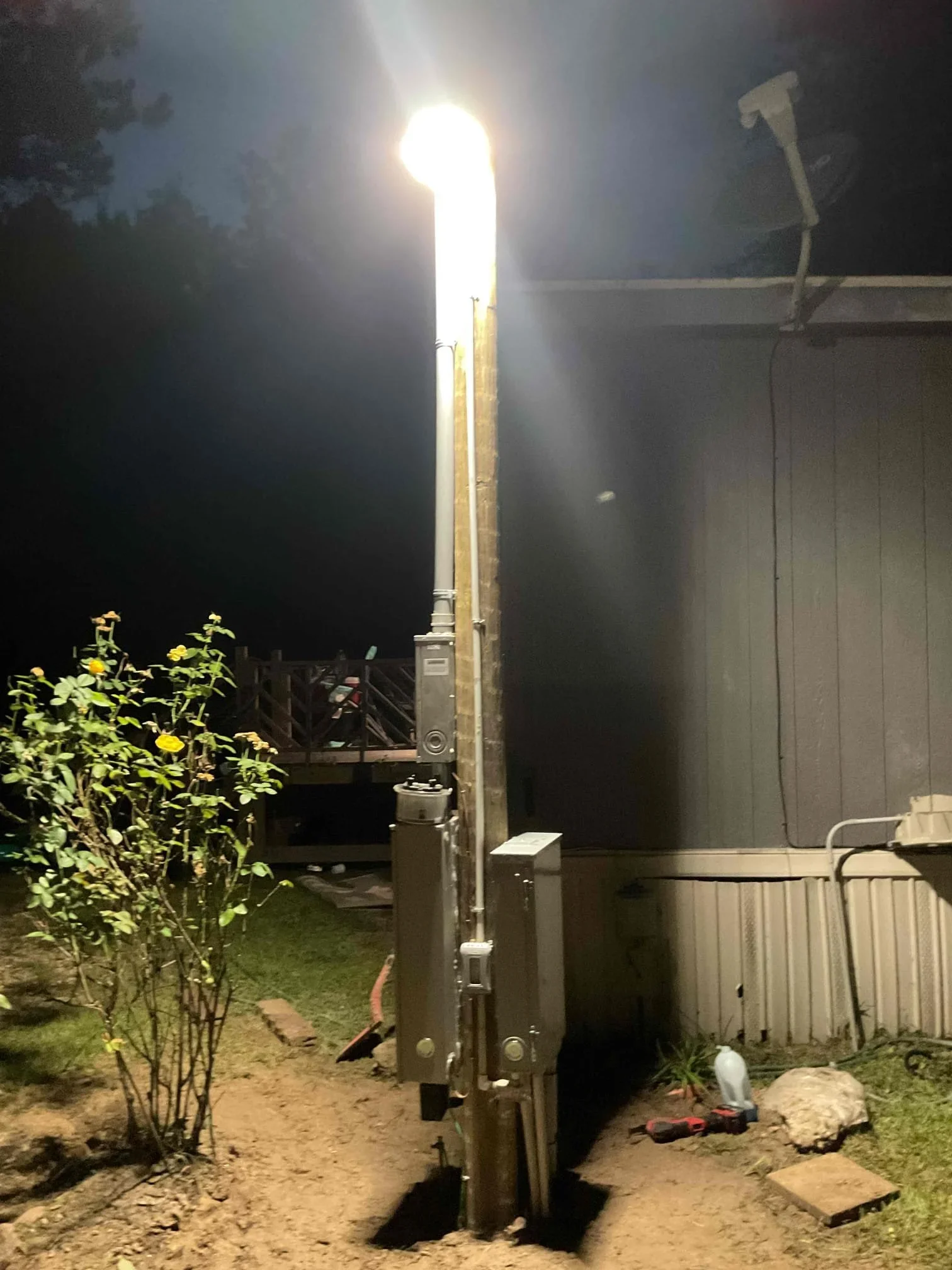 Tall metal pole with bright LED light fixture illuminating residential yard at night
