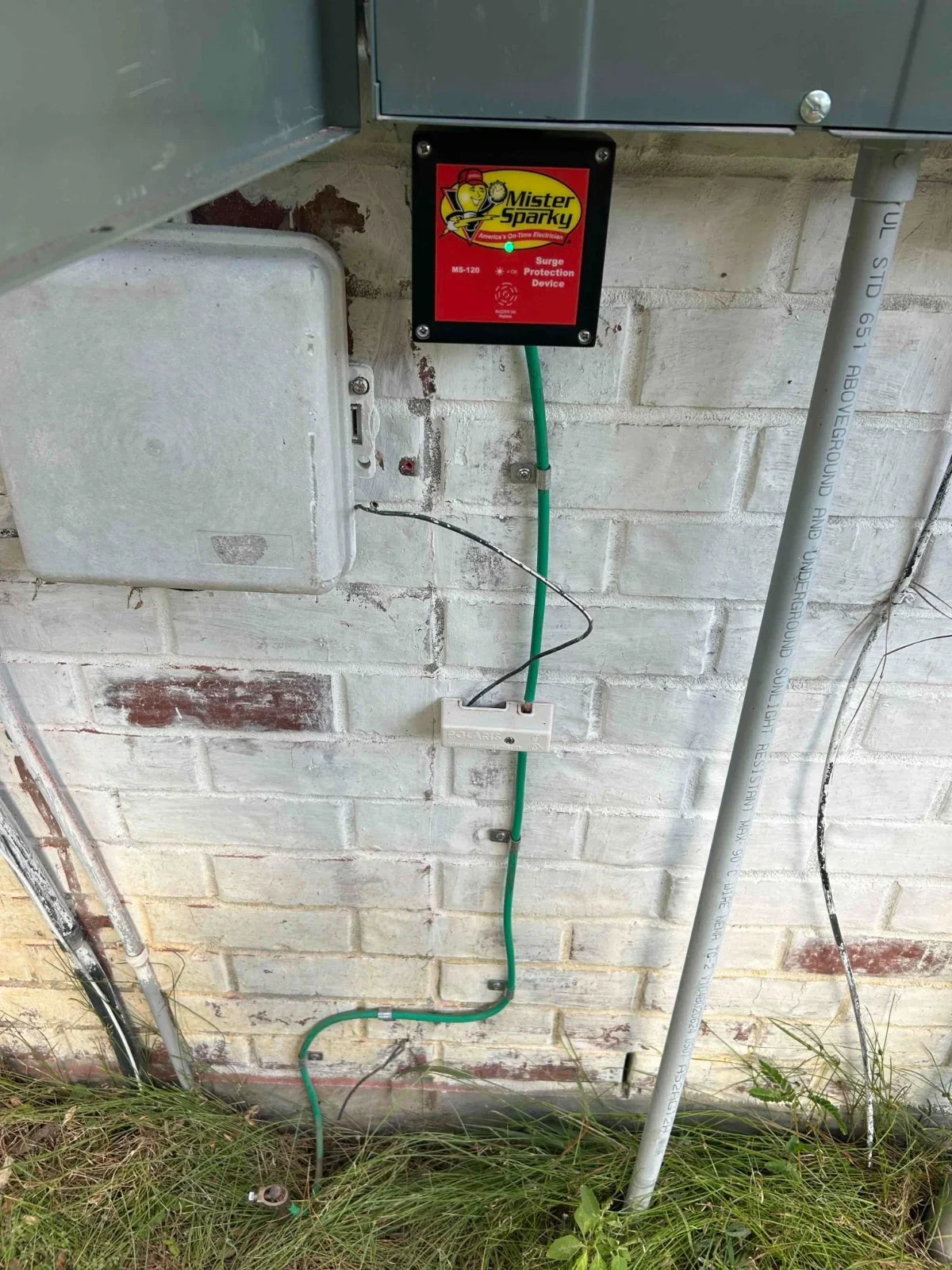 Surge protection device mounted on brick wall with green and black conduit wiring