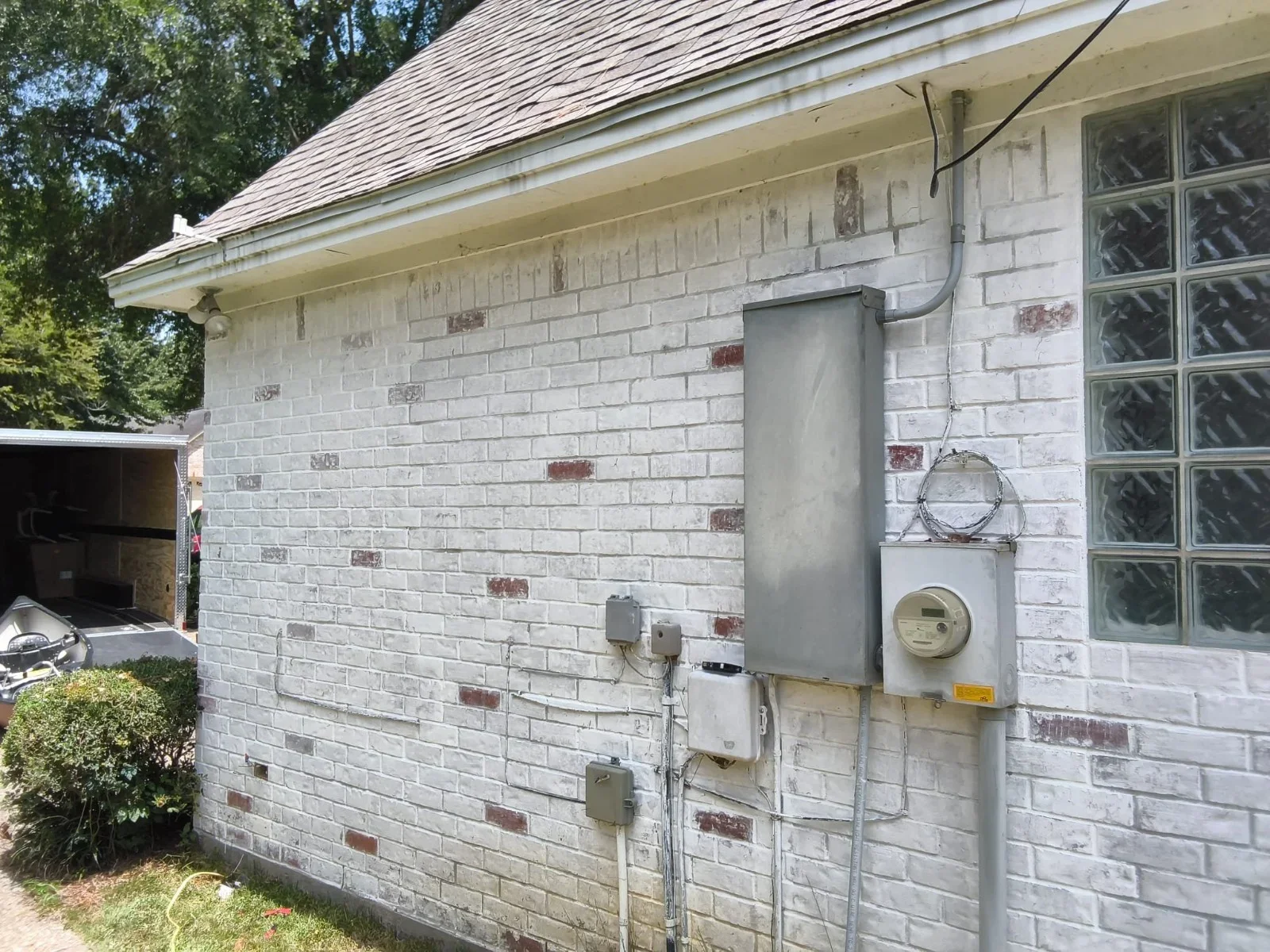 New electrical meter box and service conduit installed on white painted brick exterior wall